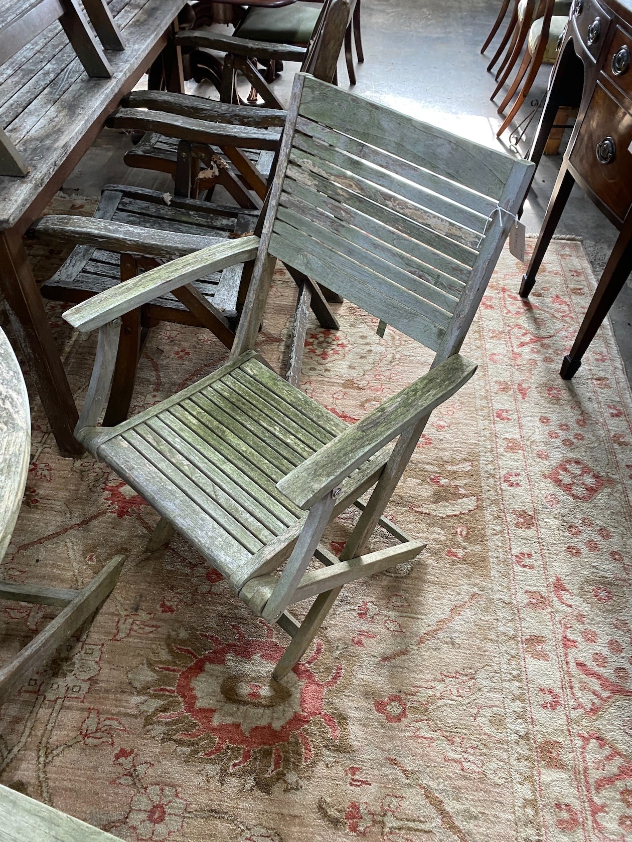 A John Lewis retailed weathered teak circular folding garden table, diameter 120cm, height 74cm and four folding elbow chairs, two with arms